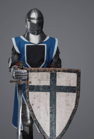 Téléchargez les photos : Chevalier médiéval en survêtement bleu tenant une épée et un bouclier, sur fond gris - en image libre de droit