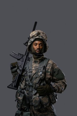 Foto de Soldado confiado en uniforme y casco de la OTAN posa con su rifle sobre un fondo gris claro, mostrando el coraje y la fuerza del personal militar - Imagen libre de derechos