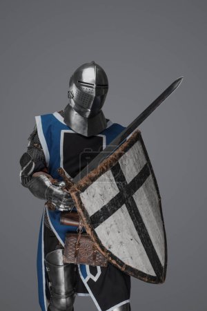 Foto de Azul vestido con sobretodo medieval caballero activamente balanceo espada en la batalla sobre fondo gris - Imagen libre de derechos