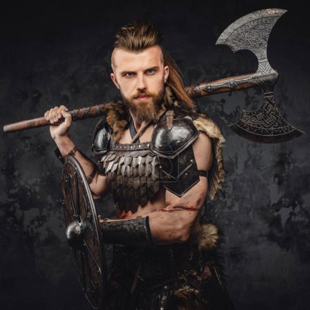 Una imagen impactante de un vikingo barbudo en pieles y armadura ligera, sosteniendo un poderoso hacha y escudo contra un telón de fondo de una pared gris texturizada