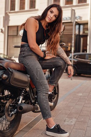 Foto de Hermosa joven con el pelo oscuro posando en una motocicleta vintage en una calle de adoquines clásico en Europa - Imagen libre de derechos