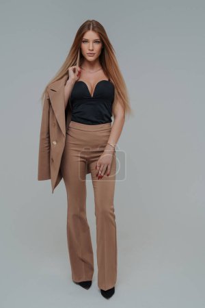 Gorgeous female model with a stunning appearance showcasing an elegant beige suit in a professional photo studio setting