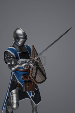 Photo for Blue surcoat-wearing medieval knight actively swinging sword in battle on gray background - Royalty Free Image