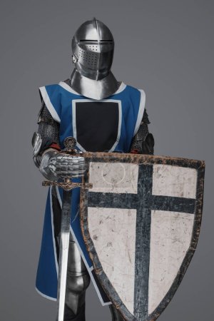 Téléchargez les photos : Chevalier médiéval coiffé d'un manteau bleu avec épée et bouclier sur fond gris - en image libre de droit