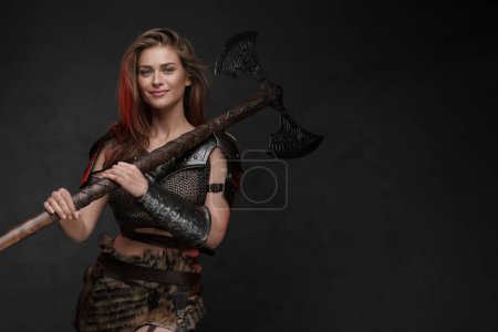 Photo for Stunning Viking girl dressed in a chainmail top and fur skirt posing with axe - Royalty Free Image