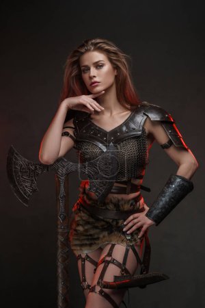 Beautiful Viking warrior model posing with a powerful axe showcasing strength and femininity in a medieval-inspired costume against a textured background