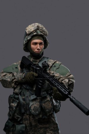 Téléchargez les photos : Un militaire armé d'un fusil et d'un casque pose prêt à l'action, affichant la discipline et la concentration des soldats en uniforme - en image libre de droit
