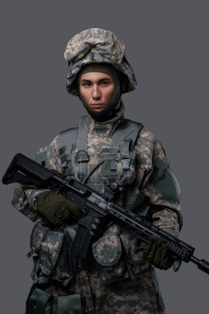 Téléchargez les photos : Jeune soldat en uniforme et casque pose avec une expression sérieuse sur un fond gris clair, mettant en valeur la force et le dévouement du personnel militaire - en image libre de droit