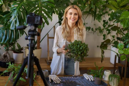 Photo for Plant-loving blogger in a white shirt and jeans, smiling in the natural light of her plant-filled urban apartment - Royalty Free Image