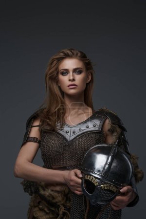 Téléchargez les photos : Un joli modèle à thème viking en armure de maille et fourrure, tenant une hache sur fond gris - en image libre de droit