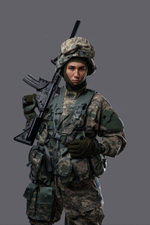 Téléchargez les photos : Jeune soldat pose avec une expression sérieuse sur fond gris clair, mettant en valeur la force et le dévouement du personnel militaire - en image libre de droit