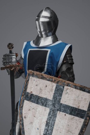 Medieval knight in blue surcoat holding a sword and shield, on grey background