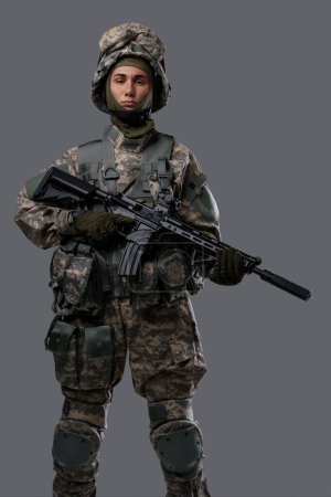 Foto de Joven en uniforme militar y casco con un rifle sobre un fondo gris - Imagen libre de derechos