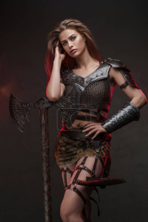 Téléchargez les photos : Magnifique modèle de guerrier viking posant avec une hache puissante et un casque mettant en valeur la force et la féminité dans un costume d'inspiration médiévale sur un fond texturé - en image libre de droit
