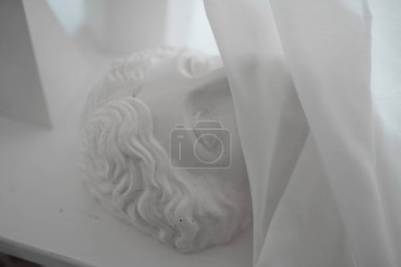 Photo for An ancient Greek plaster bust covered with a sheer veil, illuminated by soft light, resting on a table - Royalty Free Image