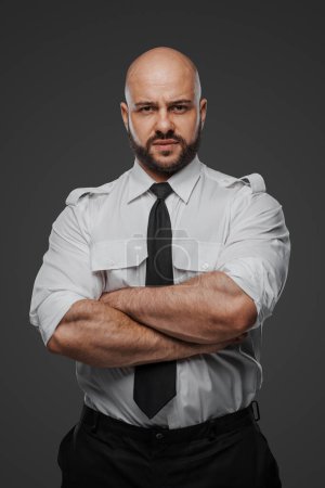 Téléchargez les photos : Homme chauve confiant avec une barbe pleine en chemise blanche et cravate, croisant les bras, symbolisant un détective, un garde du corps ou un professionnel de la sécurité sur fond de studio gris - en image libre de droit