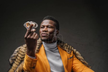 Photo for A well-dressed dark-skinned man holding a large diamond while draped in a wild animal skin on a textured background - Royalty Free Image