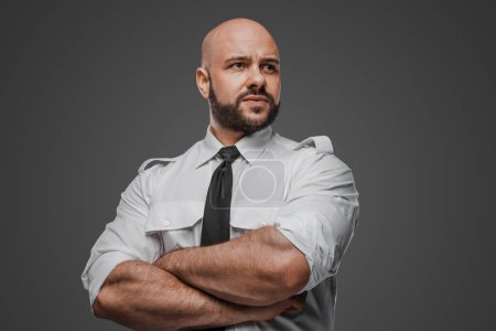 Photo for Robust bald man with beard in formal attire, confidently crossing arms, evoking themes of security, investigation, or protection against a neutral gray backdrop - Royalty Free Image