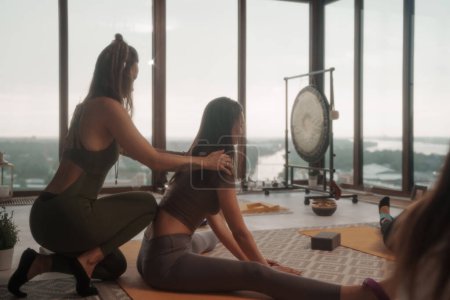 Téléchargez les photos : Groupe de femmes en vêtements de sport pratiquant le yoga et la méditation dans un appartement avec vue panoramique sur la ville - en image libre de droit