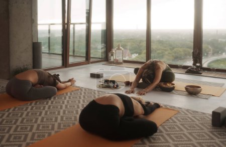 Téléchargez les photos : Femmes pratiquant le yoga et la méditation dans un cadre de groupe, portant des vêtements de sport, sur fond d'horizon de la ville - en image libre de droit