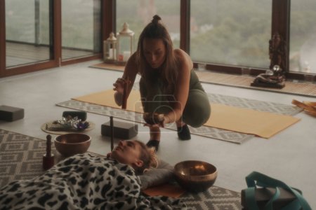 Photo for A peaceful scene of girls practicing spiritual activities and yoga using a singing Tibetan bowl, surrounded by a calming atmosphere in an apartment with a panoramic city view - Royalty Free Image