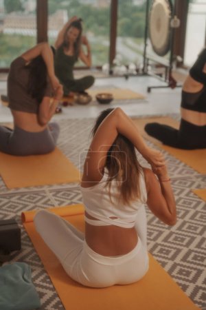 Foto de Mujeres practicando yoga y meditación en un entorno grupal, luciendo ropa deportiva, sobre un telón de fondo de un perfil urbano - Imagen libre de derechos