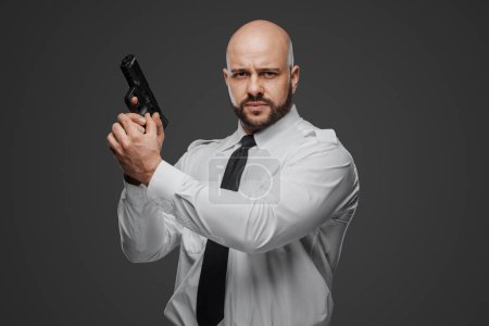 Foto de Fuerte individuo barbudo en traje blanco crujiente prepara su arma de fuego, lo que sugiere roles de seguridad o detective - Imagen libre de derechos