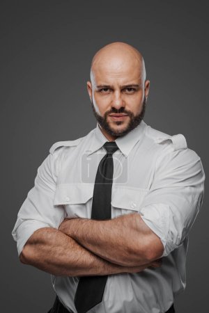 Photo for Confident bald man with a full beard in white shirt and tie, crossing arms, symbolizing a detective, bodyguard, or security professional on a gray studio background - Royalty Free Image