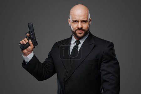 Photo for Commanding portrait of a bald, bearded gentleman with a gun, dressed sharply in formal attire - Royalty Free Image