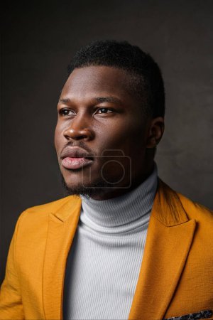 Photo for Portrait of a smartly dressed black man in a yellow blazer with short hair against a dark backdrop - Royalty Free Image