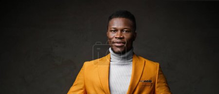 Photo for Portrait of a smartly dressed black man in a yellow blazer with short hair against a dark backdrop - Royalty Free Image