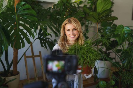 Foto de Elegante florista y blogger capturando su rutina de cuidado de plantas en la habitación con una vibrante vegetación - Imagen libre de derechos