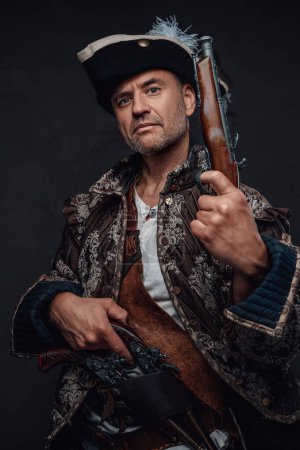 Photo for Pirate showcasing his seasoned look, wearing a brown vest and sporting two single-handed muskets against a textured grey wall - Royalty Free Image