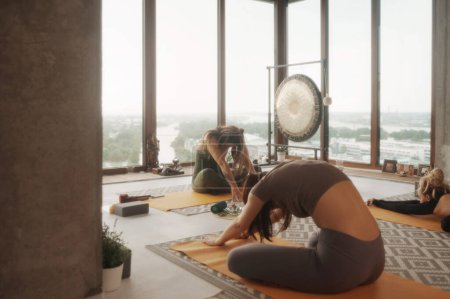Foto de Grupo de mujeres en ropa deportiva practicando yoga y meditación en un apartamento con vistas panorámicas a la ciudad - Imagen libre de derechos