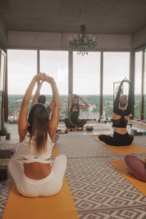 Photo for Group of girls practicing yoga and meditation in a city apartment with panoramic views - Royalty Free Image