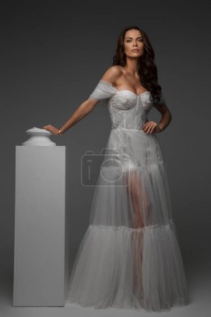 Photo for Elegant woman in white gown juxtaposed with classical Greek statues in a studio setting - Royalty Free Image