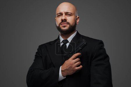 Téléchargez les photos : Portrait d'un homme chauve, barbu et armé, vêtu d'une tenue formelle - en image libre de droit
