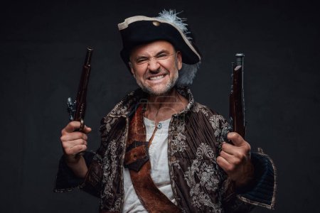 Foto de Un personaje pirata amenazante, envejecido y rugoso, luciendo una barba salvaje, chaleco y sombrero, blandiendo dos mosquetes frente a un fondo oscuro y texturizado - Imagen libre de derechos