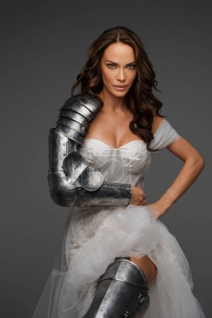 Photo for Fashion meets history: Brunette in luxurious dress and armor pieces on a neutral background - Royalty Free Image