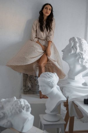 Téléchargez les photos : Portrait complet d'un modèle brune saisissant au milieu de statues grecques dans un atelier de sculpteurs - en image libre de droit