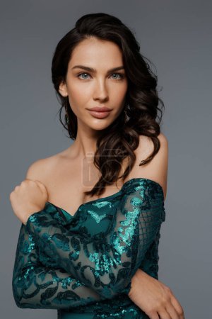 Téléchargez les photos : Élégant modèle brune dans une riche robe de soirée verte, mettant en valeur sa coiffure luxuriante sur un fond gris - en image libre de droit