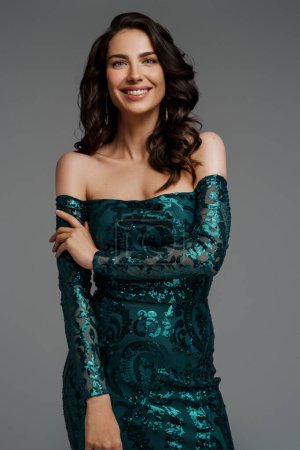 Photo for Breathtaking brunette with a charming smile, lavish hairstyle in an elegant green evening gown against a gray background - Royalty Free Image