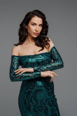 Photo for Stunning brunette with a voluminous hairstyle in a graceful green evening gown against a gray backdrop - Royalty Free Image