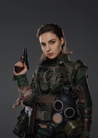 Téléchargez les photos : Portrait d'une femme soldat en uniforme militaire avec un pistolet, incarnant un rebelle ou un partisan dans un conflit au Moyen-Orient sur fond gris - en image libre de droit