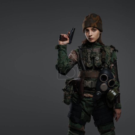 Foto de Retrato de una soldado con uniforme militar y gorra, con una mano vendada y una pistola, retratando a un rebelde o partisano en un conflicto en el Medio Oriente, sobre un fondo gris - Imagen libre de derechos