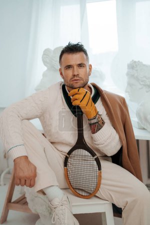 Téléchargez les photos : Dapper homme en vieille tenue de style argent frappant une pose avec une raquette de tennis - en image libre de droit