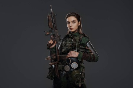Photo for Portrait of a female soldier in military attire, holding a homemade automatic rifle, depicting a rebel or partisan in a Middle Eastern conflict against a gray background - Royalty Free Image