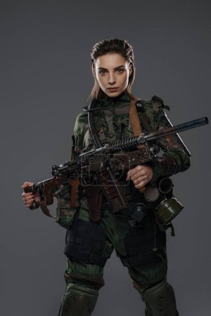 Retrato de una soldado con atuendo militar, sosteniendo un rifle automático hecho en casa, que representa a un rebelde o partisano en un conflicto de Oriente Medio sobre un fondo gris