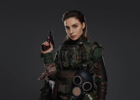 Téléchargez les photos : Portrait d'une femme soldat en uniforme militaire avec un pistolet, incarnant un rebelle ou un partisan dans un conflit au Moyen-Orient sur fond gris - en image libre de droit
