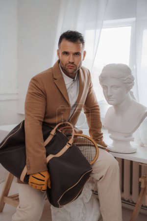 Foto de Hombre rico en estilo de dinero viejo sosteniendo una bolsa y raqueta de tenis en el estudio de escultores - Imagen libre de derechos